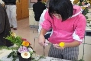 切り花を手に持ちフラワーアレンジメントに挑戦する児童の写真