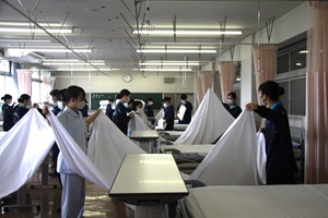 生徒が2人1組になりシーツの畳み方を練習している様子