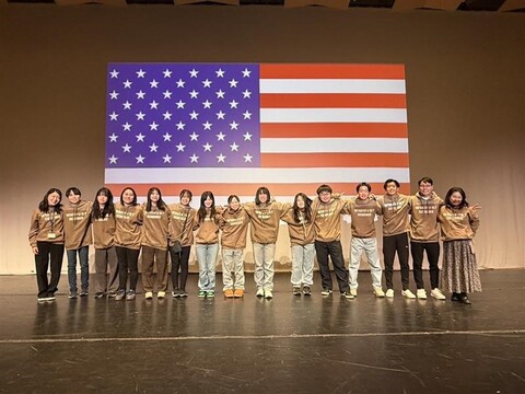 海外姉妹校でプレゼンテーションをしている際にアメリカ国旗の前で撮影した画像